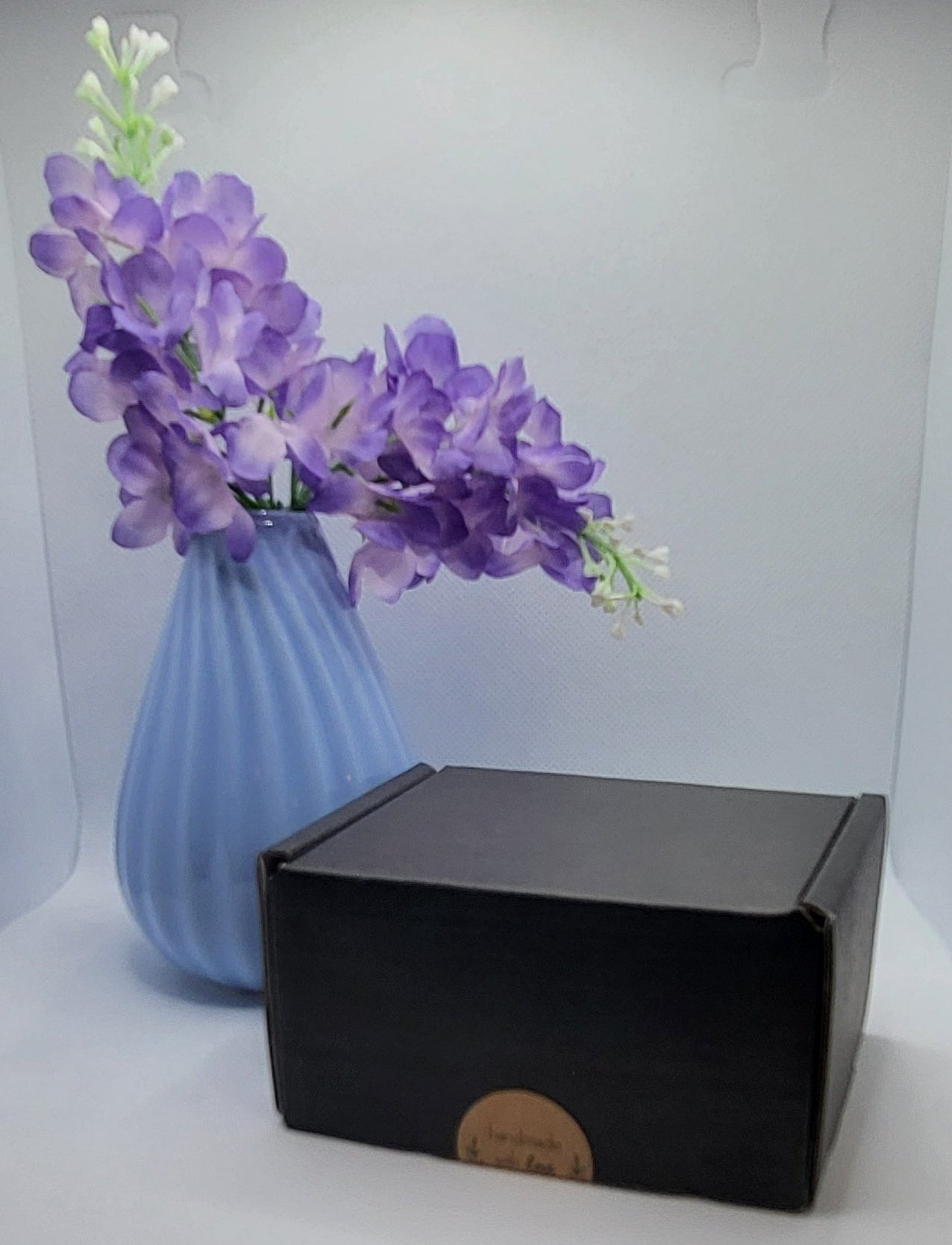 Blue vase with purple flowers on a white background with a black box.